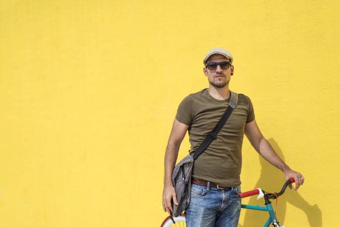Man in hat and sunglasses standing with bike next to yellow wall