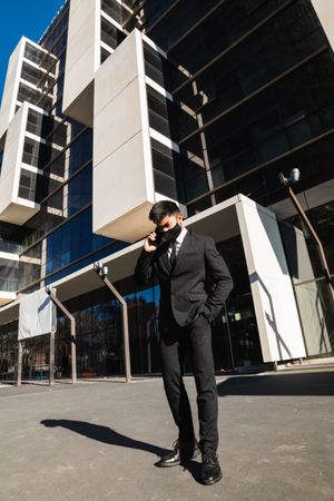 Businessman in mask speaking on smartphone in city