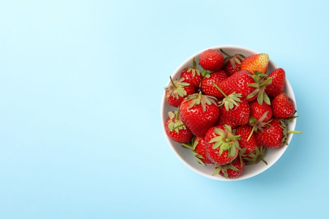 Bowl with tasty strawberry on blue background. Summer berry