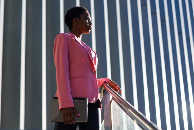 Female wearing suit with pink jacket outside office with striped shadows