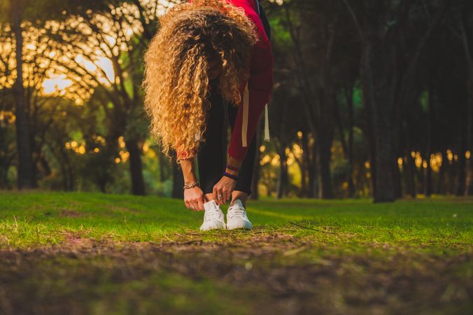 Sportive curly woman bending forward on lawn