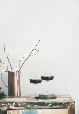 Wine glasses with dried cotton in vase, on light background, vertical composition, copy space