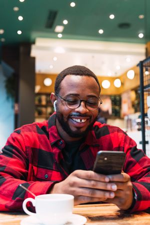 Cheerful Black man with smartphone in cafe