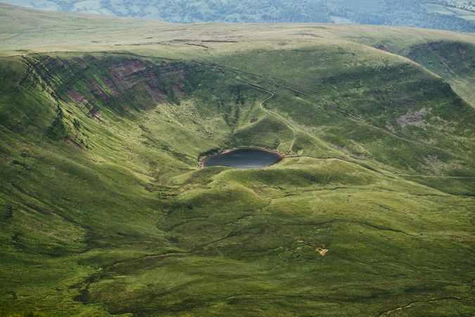 Look down at a small lake nestled in grassy mountains in Wales