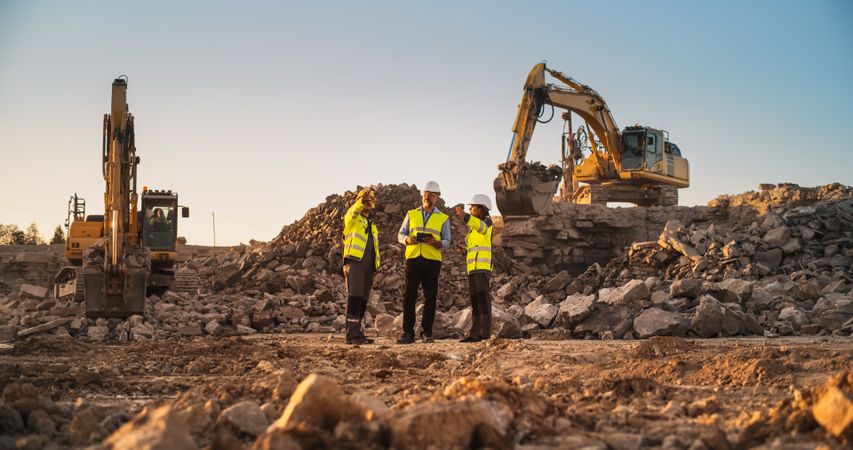 Construction Site With Excavators on Sunny Day: Diverse Team Of Male And Female Specialists Discussing Real Estate Project. Civil Engineer, Architect And Investor Talking About New Apartment Building.