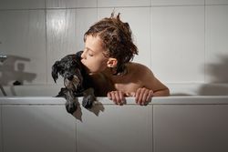 Boy kissing dog in bathtub