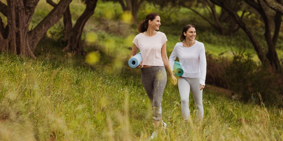 Smiling fitness women walking with yoga mats in a park
