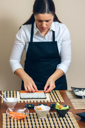 Female chef placing salmon into on rice as she makes fresh sushi rolls