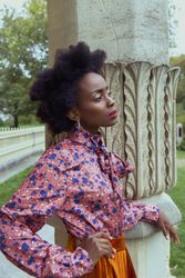 Side view of woman in blue and pink floral top and brown skirt standing beside pillar outdoor