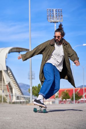 Positive adult stylish dressed man riding skateboard in park
