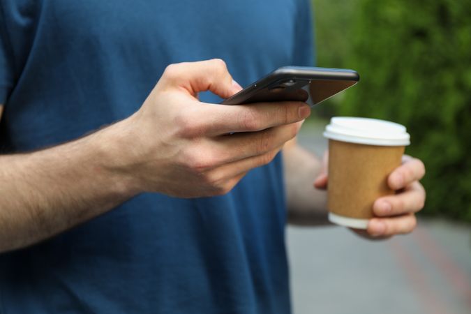 Young man holds phone and cup of coffee, close up
