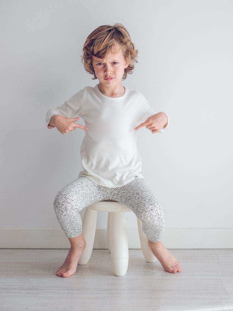 Boy in white pajamas leaning against the white wall of his house.