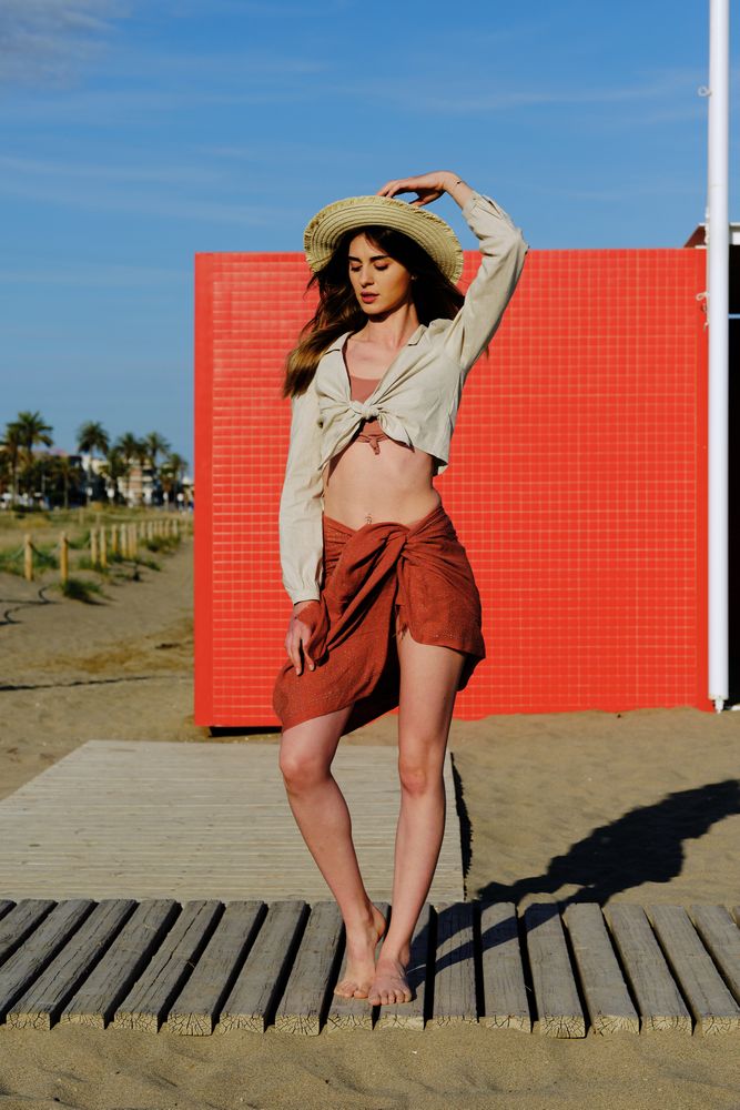 A long hair fashion model with a hat at the beach in front of a red wall