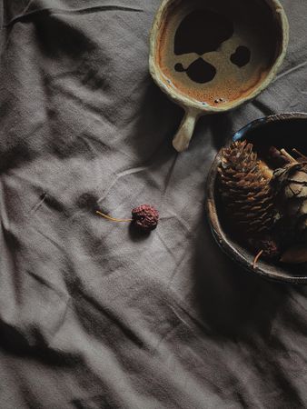 Top view of coffee and bowl of pine cones on grey sheets with copy space