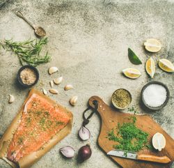 Salted salmon fillet with fresh herbs, limes, onions, bread board, square crop, copy space