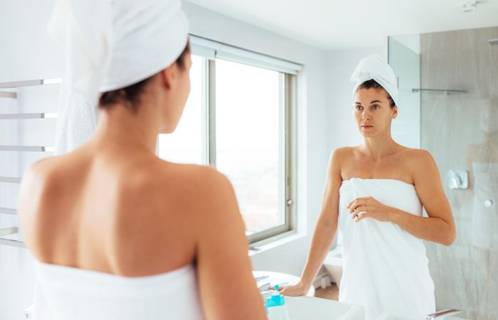 Woman standing in front of mirror in bathroom in a towel