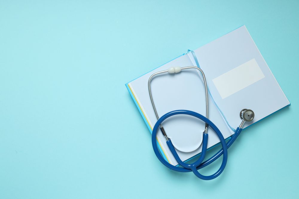 Notepad and stethoscope on blue background, space for text