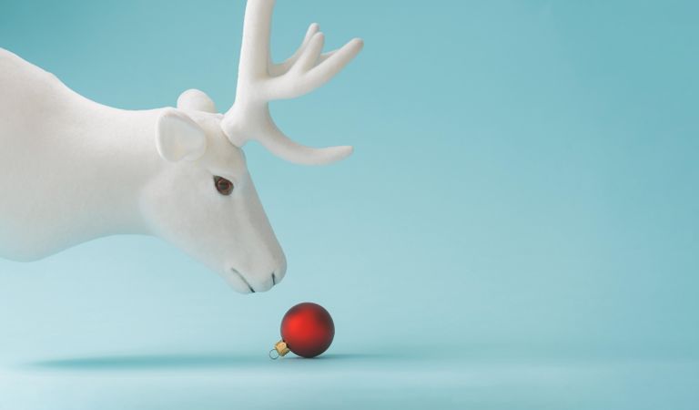 Reindeer with red Christmas bauble decoration on pastel blue background