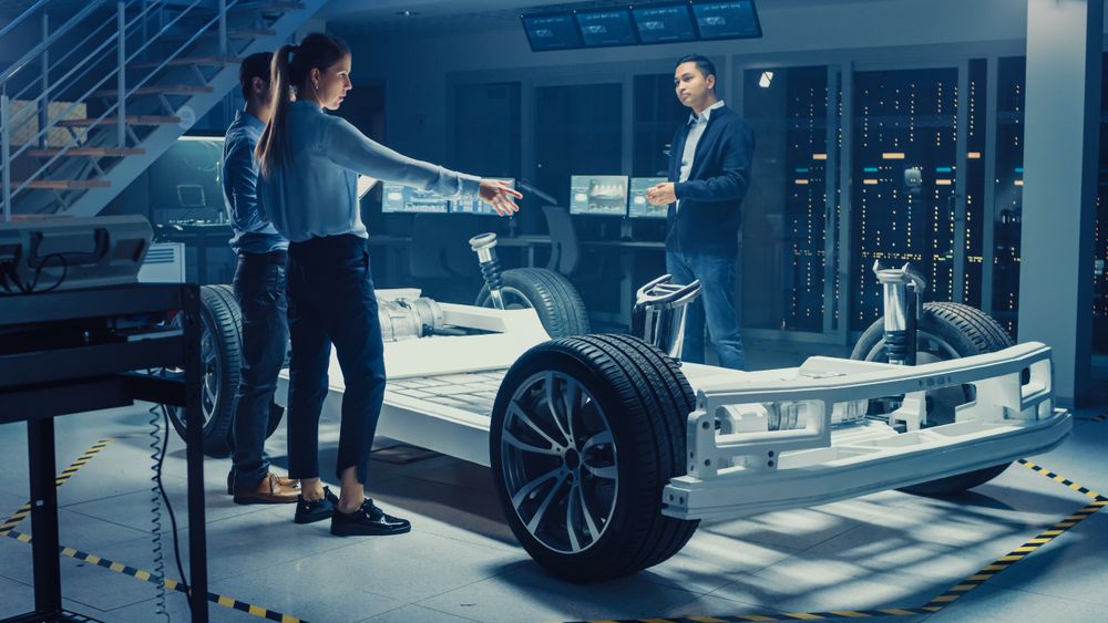 Automotive Design Engineers Talking while Working on Electric Car Chassis Prototype.