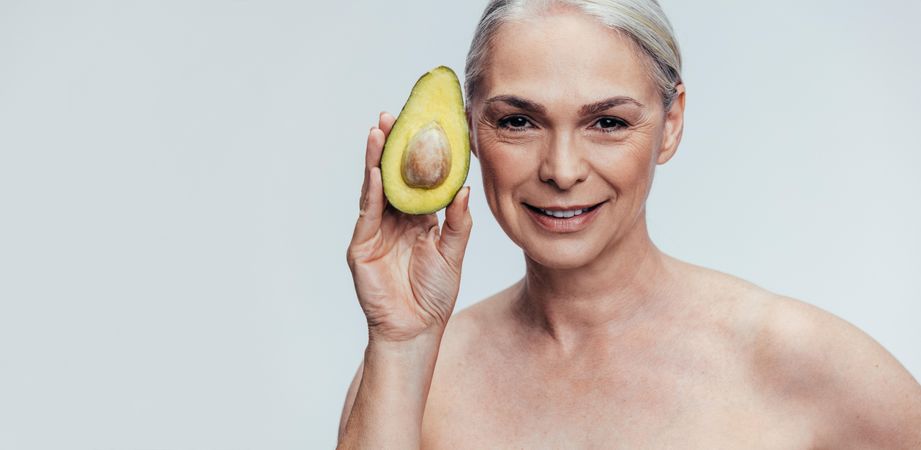 Mature woman holding up an avocado and looking at camera