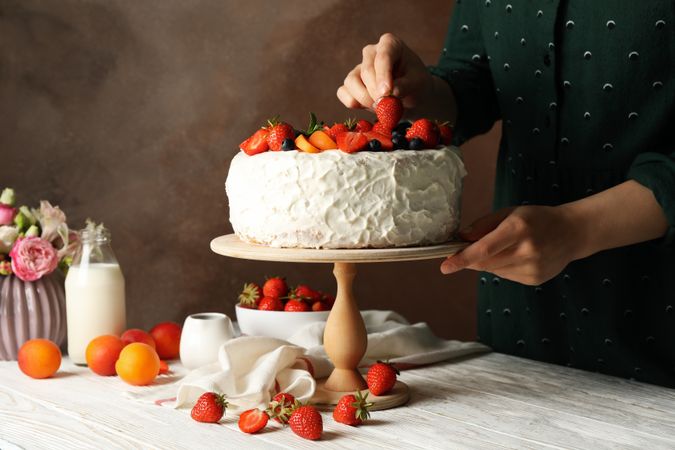 Woman puts strawberry on berry cream cake. Delicious dessert