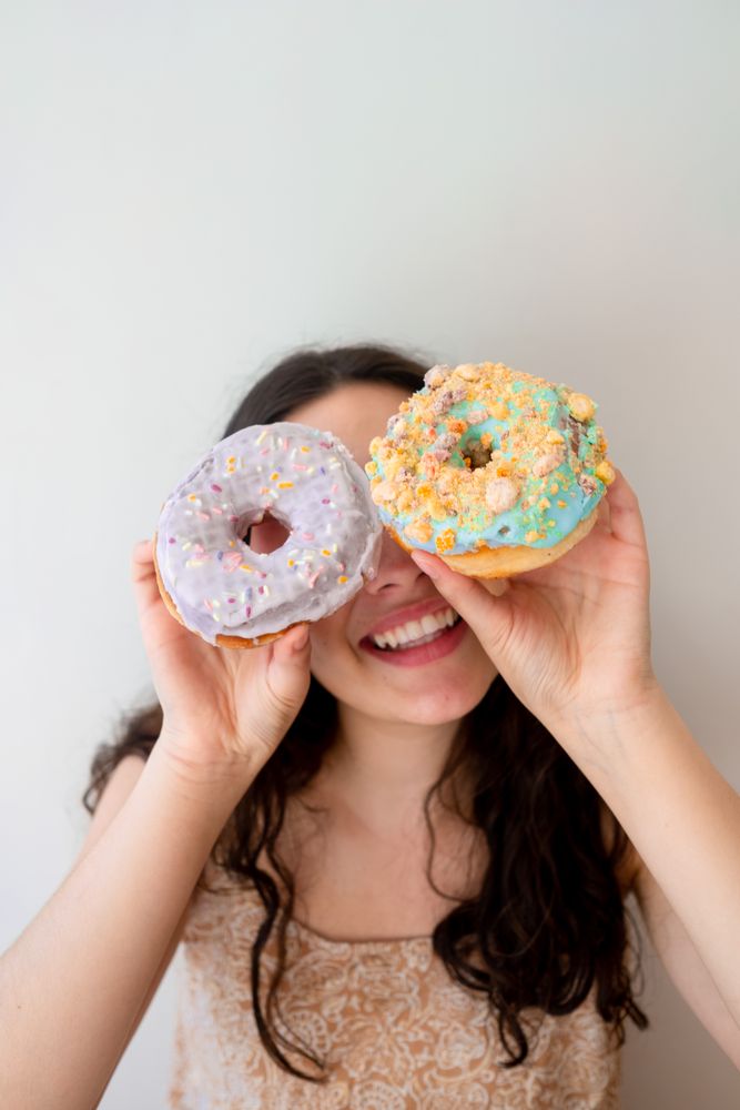 Playful woman making glasses of donuts while standing by white wall