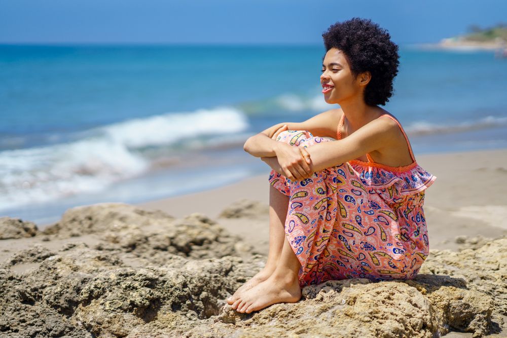Happy woman sitting on the rocks on the coast looking out to the sea