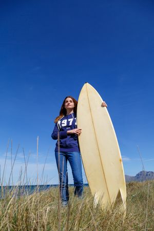 Woman with surfboard in seaside with dry vegetation