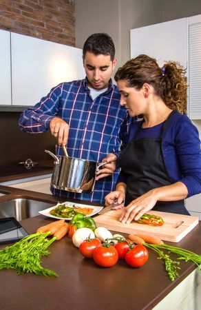 Woman cutting vegetables while her husband shows her the pot