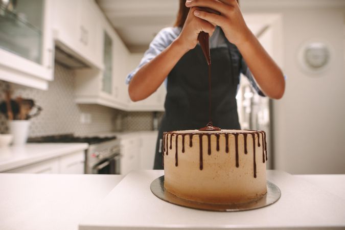 Cropped shot of woman squeezing chocolate sauce on cake