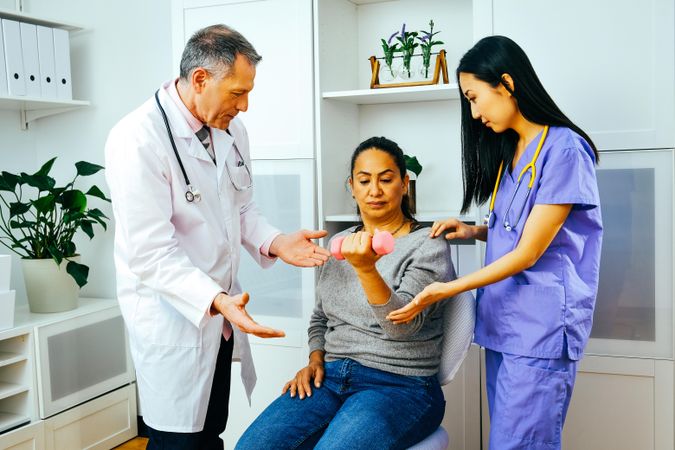 Serious doctor and physiotherapist helping patient with arm rehab exercises