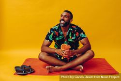 Black male sitting on towel and looking away while holding up tropical drink 4jLNR0
