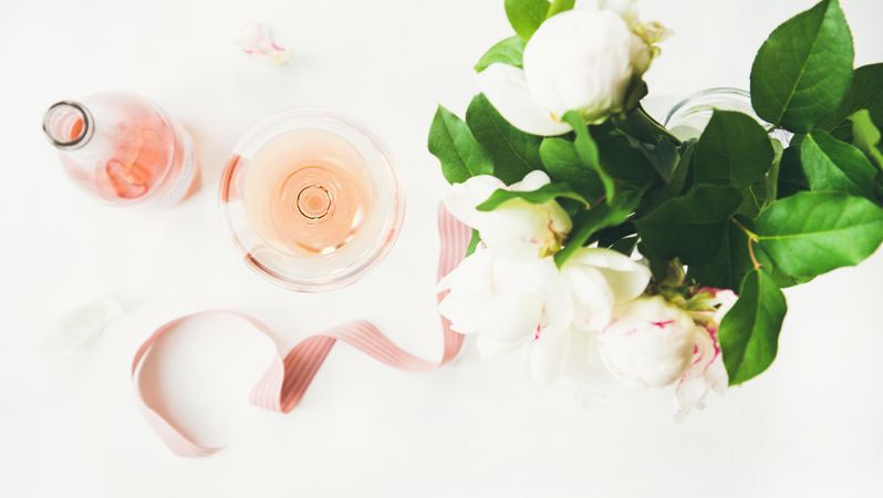 Top view of glass of pink rose wine, and bottle with flowers and ribbon, horizontal composition