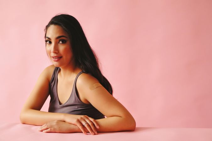 Pensive Hispanic woman looking away from camera and sitting in pink room, copy space