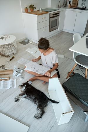 Woman examining manual near dog while assembling furniture