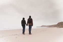 Couple walking on sand shore near water