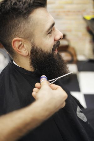 Man having his beard trimmed by barber’s scissors