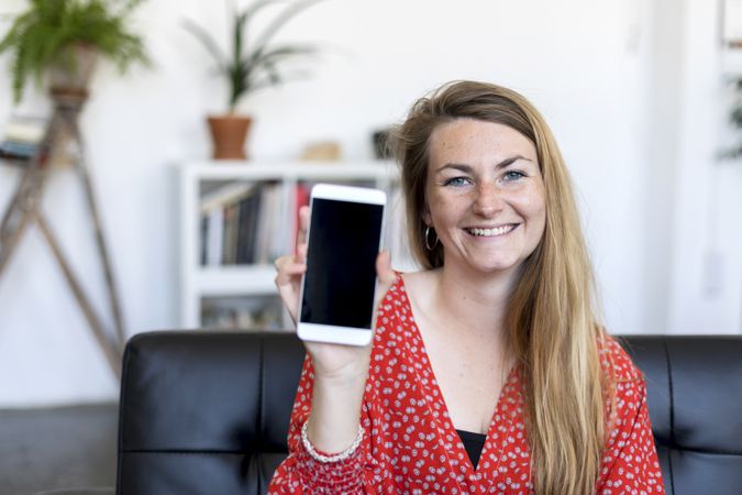 Woman showing a screen of a smart phone sitting on a sofa