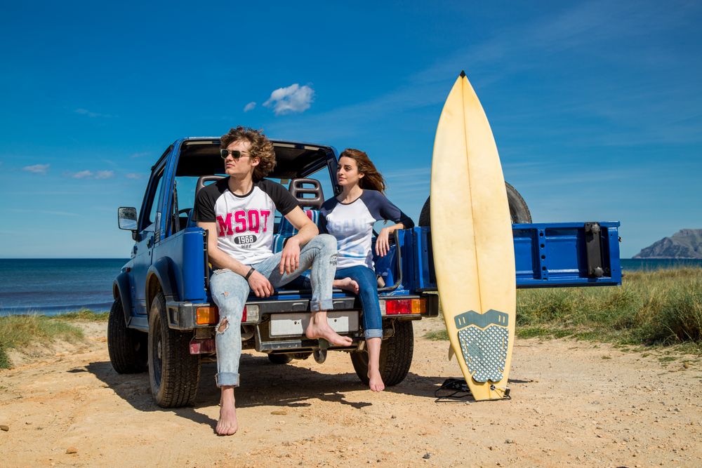 Couple with surfboard sitting on a car