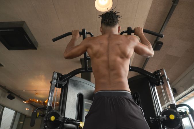 Muscular guy doing pull ups on exercise machine