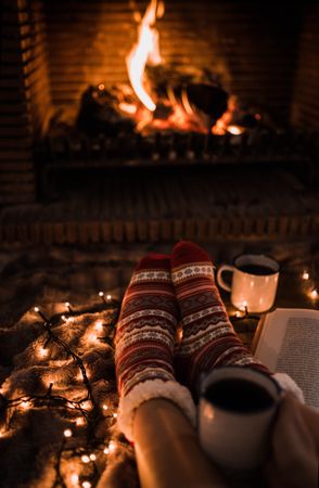 Crop legs with book near fireplace