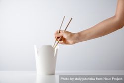 A person reaching into a to go container with chopsticks 5ndnmb