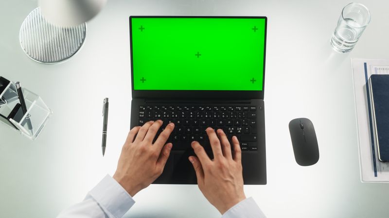 Anonymous Office Worker Typing on a Laptop Computer with Mock Up Green Screen Chromakey Display with Motion Tracker Placeholders. Manager Corresponding with Business Partners by Email. Top Down View