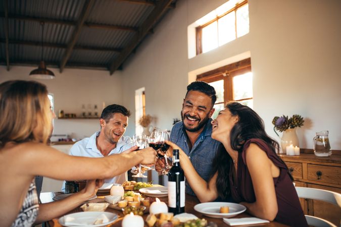 Friends toasting with glasses of red wine at dinner table