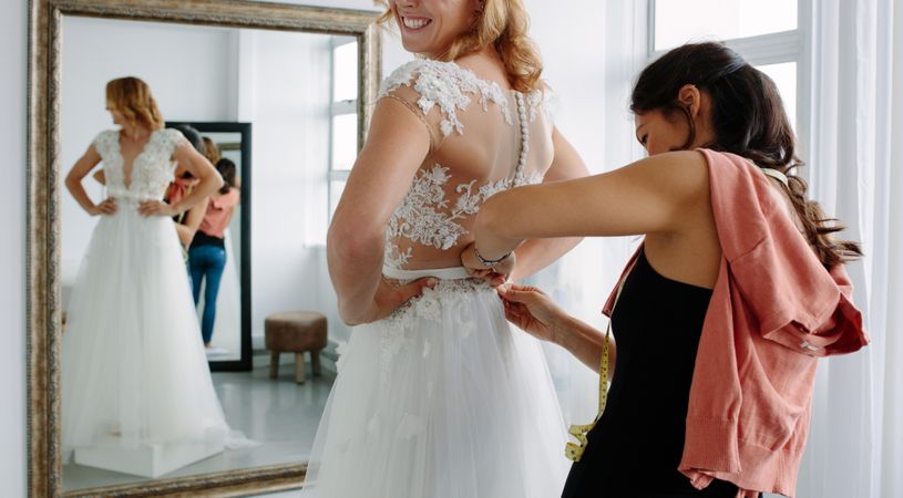 Female trying on wedding dress in a shop with women assistant