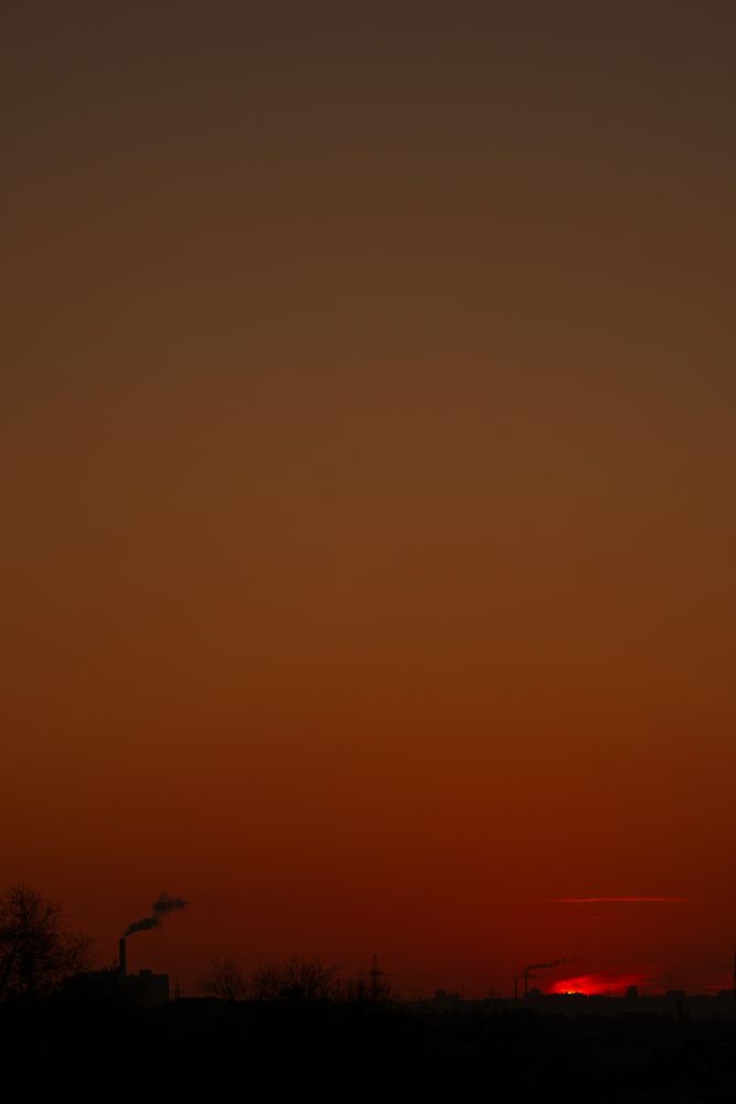 Dark orange skyline with factory smoke twilight hour