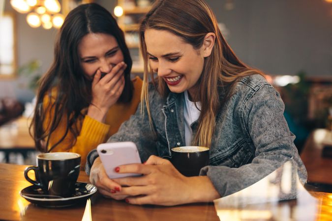 Happy female friends using at phone at cafe and smiling