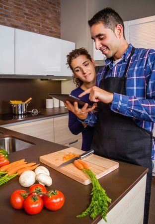 Couple reading digital tablet for instruction while prepping dinner