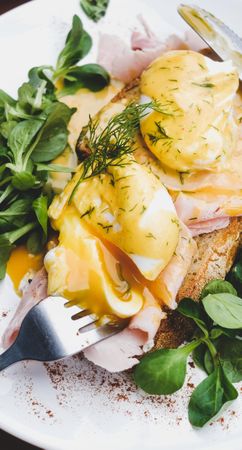 Eggs Benedict with yoke broken with greens, coffee, top view, narrow composition