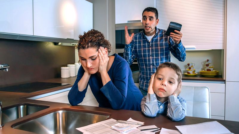 Couple in conflict in front of son with bills strewn on the kitchen counter